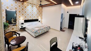 A hotel room with a bed, a desk, a chair, a mirror, a ceiling fan, and a wardrobe. - Hotel Buddha Park (Varanasi)