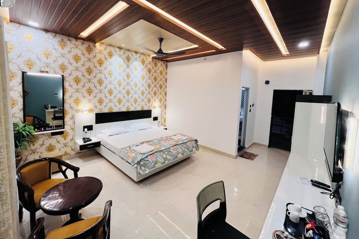 A hotel room with a bed, a desk, a chair, a mirror, a ceiling fan, and a wardrobe.