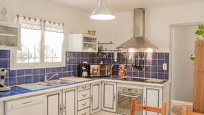 A kitchen with blue tiles, white cabinets, a stainless steel range hood, and a wooden dining table. - One-storey villa with air conditioning and pool (Bagnols en Forêt)