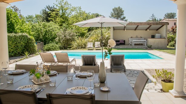 A patio with a table set for dining, overlooking a swimming pool and lush greenery. - One-storey villa with air conditioning and pool (Bagnols en Forêt)