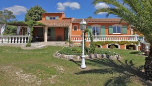 A two-story house with a tiled roof, a balcony with a white balustrade, and a garden with a palm tree. - Child-friendly holiday home with pool (Bagnols en Forêt)