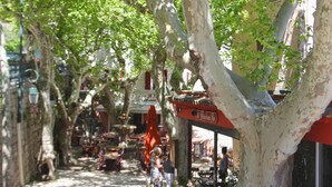 A tree-lined street with outdoor seating and a building with a red awning. - Child-friendly holiday home with pool (Bagnols en Forêt)