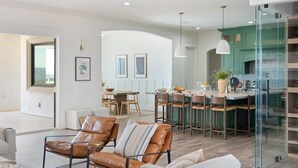 A modern kitchen with green cabinets, a central island, and pendant lighting. There is a dining area with a table and chairs, and a living space with leather chairs and a sofa. - PInot Point by AvantStay | Valley Estate Mins to Wineries | Pool + Home Theater (Temecula)