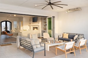 A modern living room with a fireplace, a ceiling fan, and a large window.