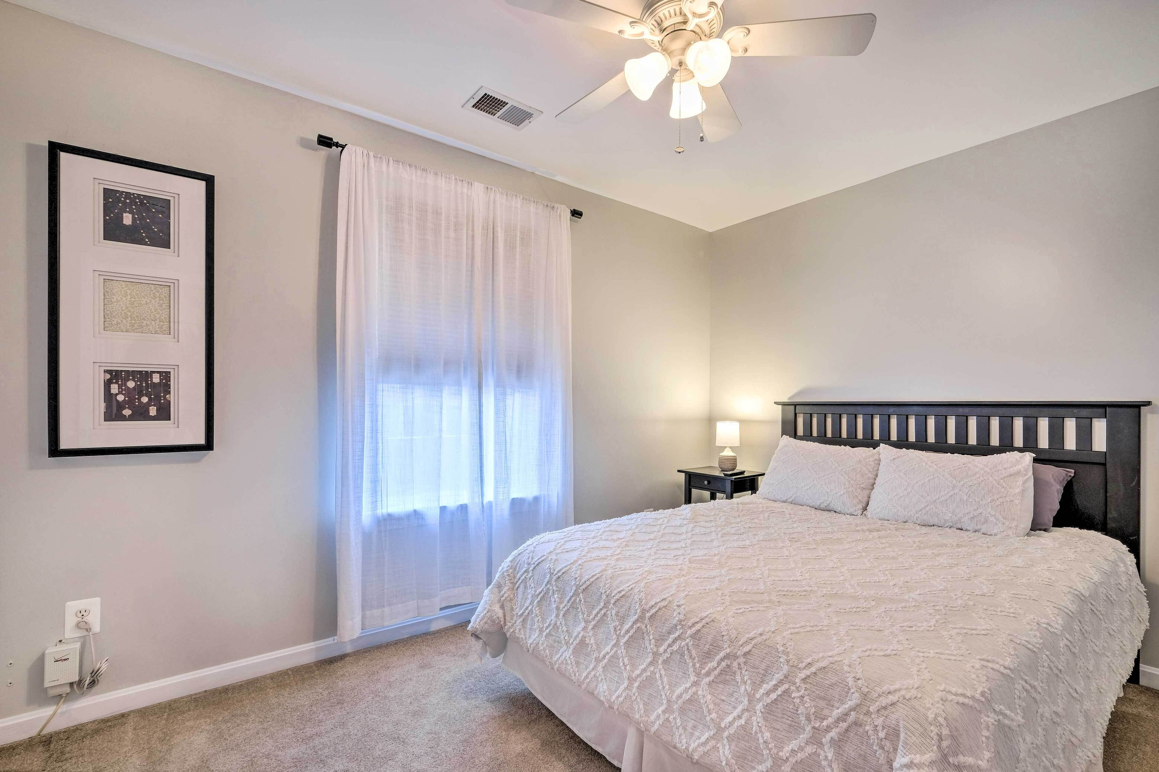 A bedroom with a bed, a ceiling fan, a nightstand, and a window with curtains.