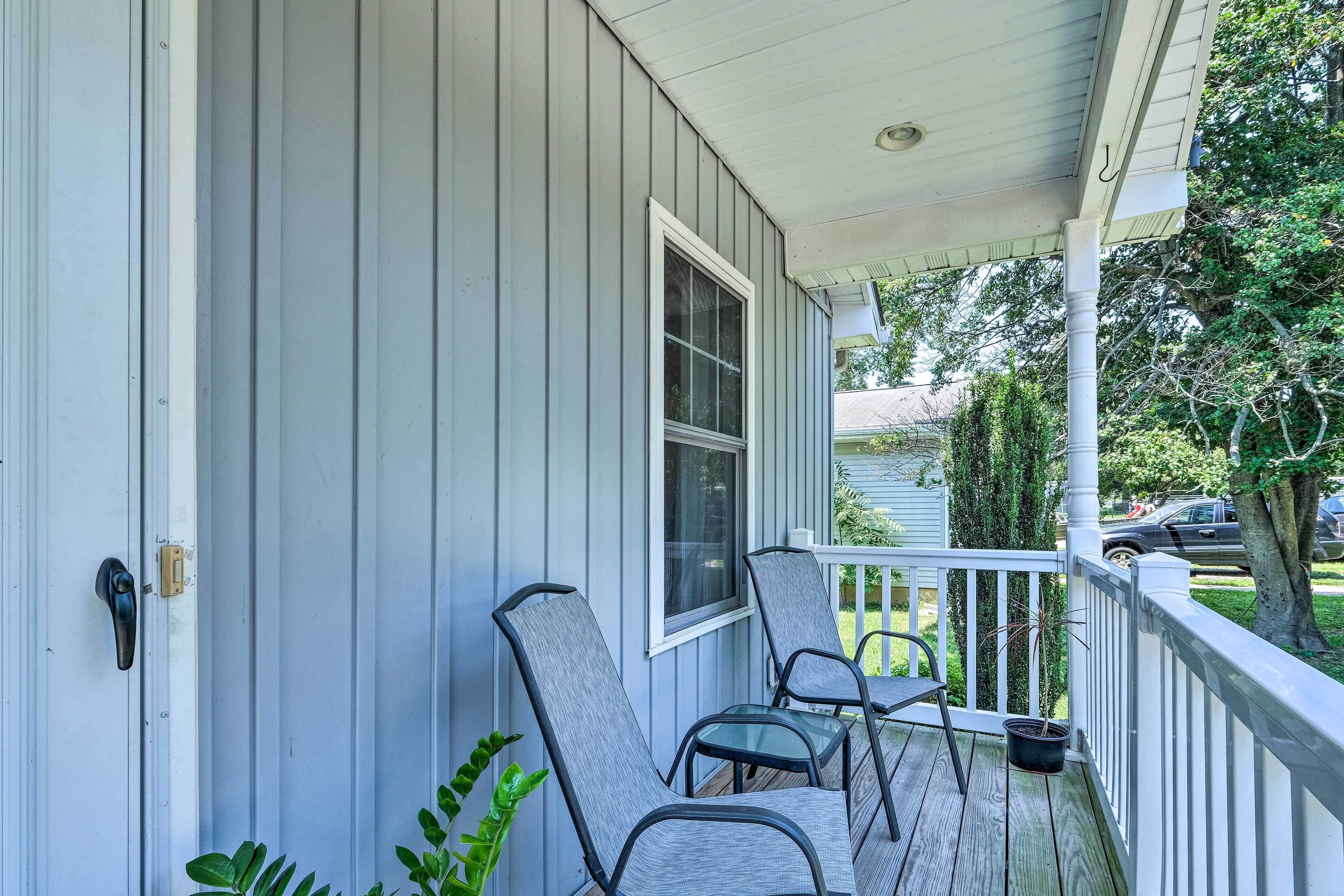 A porch with two chairs and a table, a white railing, and a potted plant.