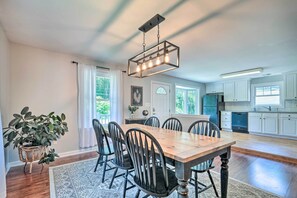 A spacious dining area with a wooden table and chairs, a hanging light fixture, and a view of the kitchen in the background. - Idyllic Pasadena Retreat with Garden + Hot Tub! (Pasadena)