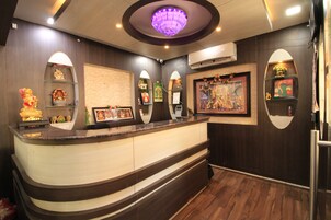 A reception area with a curved counter, wall-mounted shelves with decorative items, a large framed painting, and a ceiling light fixture.