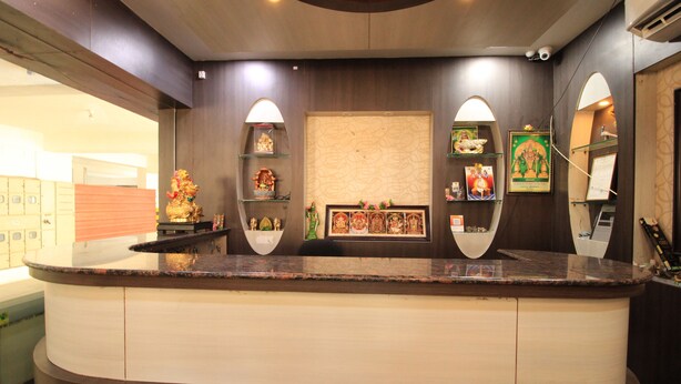 A reception area with a curved counter, shelves with decorative items, and a wall-mounted screen. - Viswa Service Apartments (Madurai)