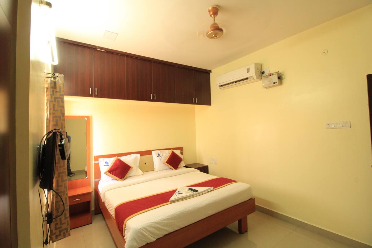 A hotel room with a bed, a wardrobe, an air conditioning unit, and a ceiling fan.