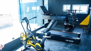 A gym with exercise equipment including a treadmill, stationary bike, and elliptical machine. - Viswa Service Apartments (Madurai)