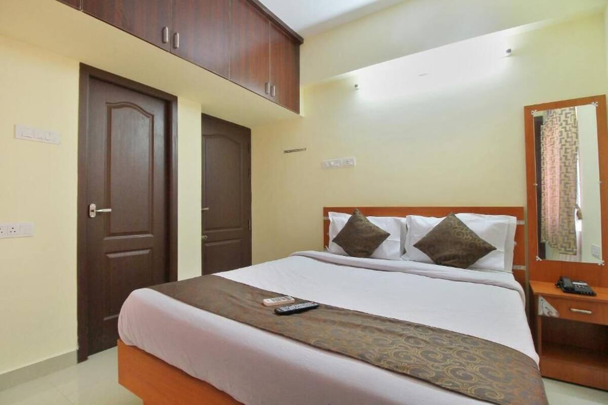 A hotel room with a bed, a bedside table with a phone, and a mirror on the wall.