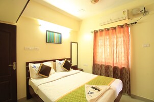 A hotel room with a bed, a mirror, a window with curtains, and an air conditioning unit on the wall.
