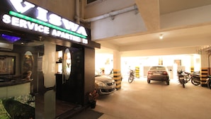 A service apartment entrance with a neon sign, a car, and motorcycles parked inside. - Viswa Service Apartments (Madurai)