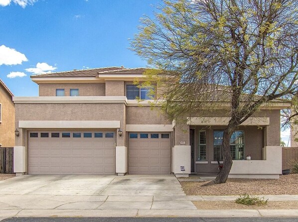 A two-story house with a garage, a tree in front, and a clear sky.