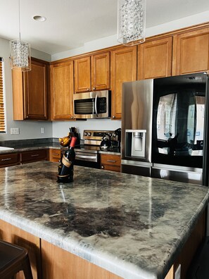 A kitchen with wooden cabinets, stainless steel appliances, a marble countertop, and a wine bottle.