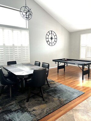 A spacious room with a dining table, chairs, a pool table, and two wall clocks.