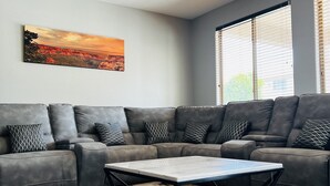 Ein modernes Wohnzimmer mit einem grauen Ecksofa, einem Couchtisch und einem Deckenventilator.