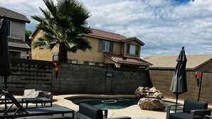 Ein Garten mit Pool, Terrassenmöbeln, einer Palme und einem Haus mit Ziegeldach.