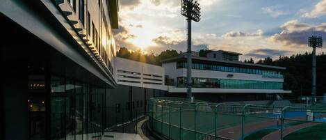 A modern building with a glass facade, a sports field, and a bicycle parked in front.