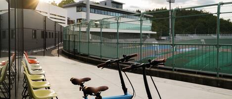 A row of yellow chairs and a red and blue bicycle parked near a sports field.