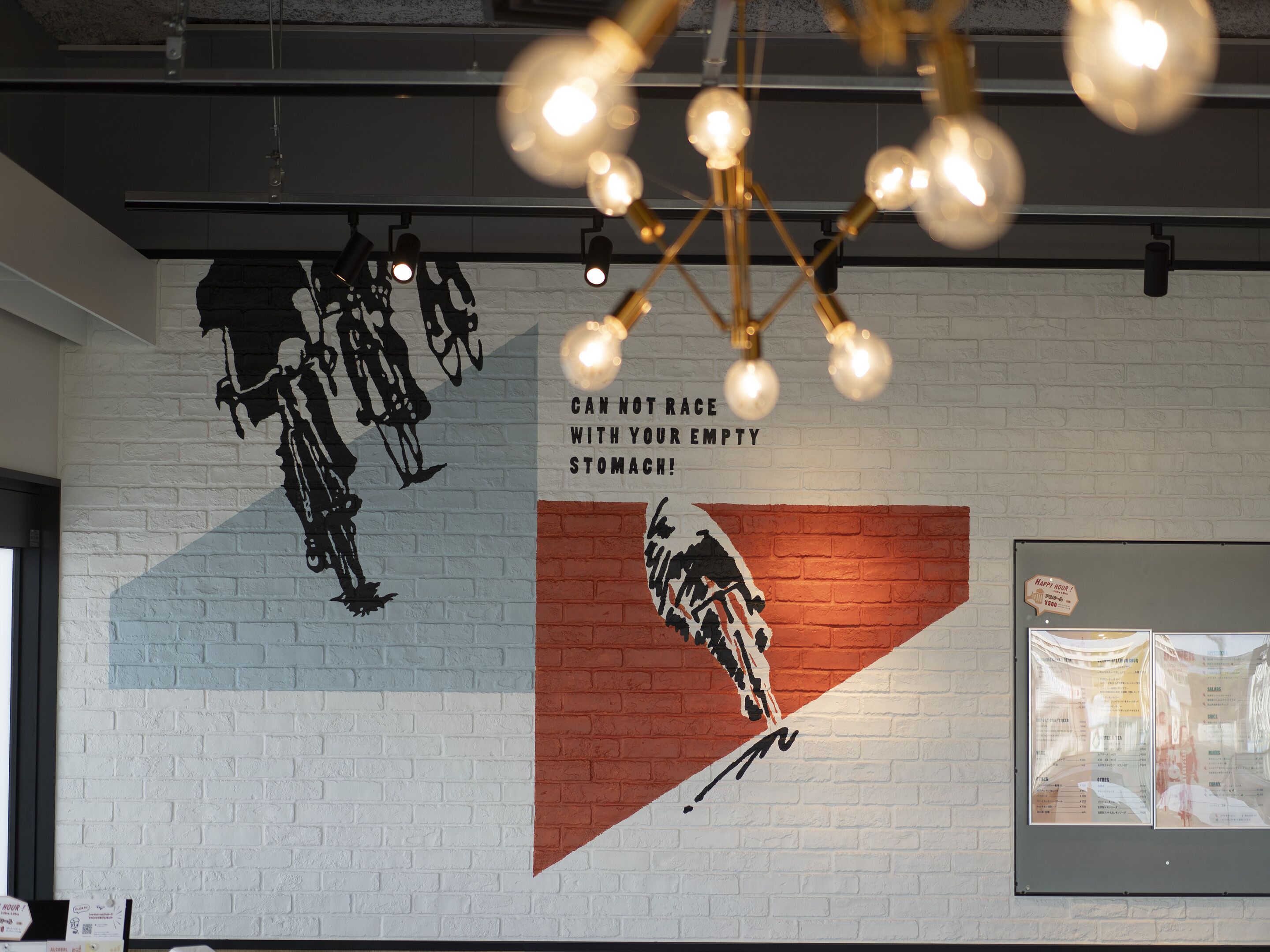 A restaurant interior with a mural, hanging lights, and a menu board.