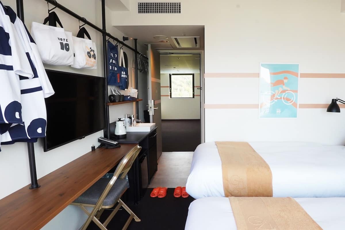 A hotel room with two beds, a desk with a chair, a mirror, and a wardrobe.