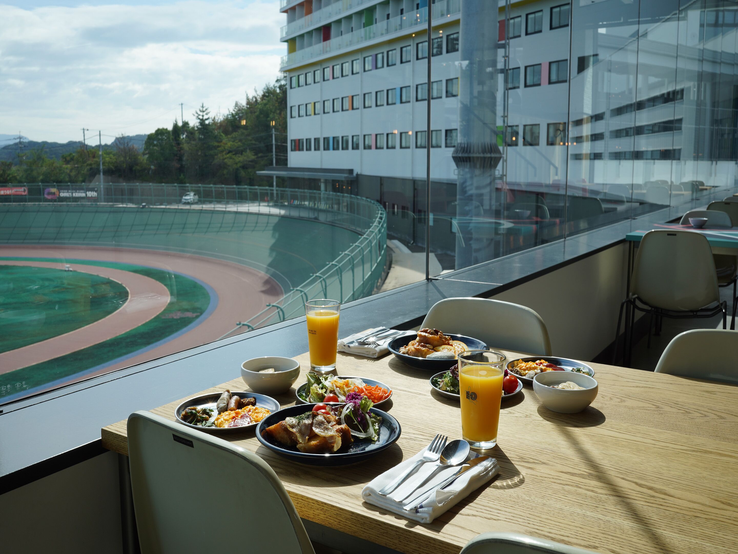 A dining table with various dishes and a glass of orange juice, overlooking a stadium.