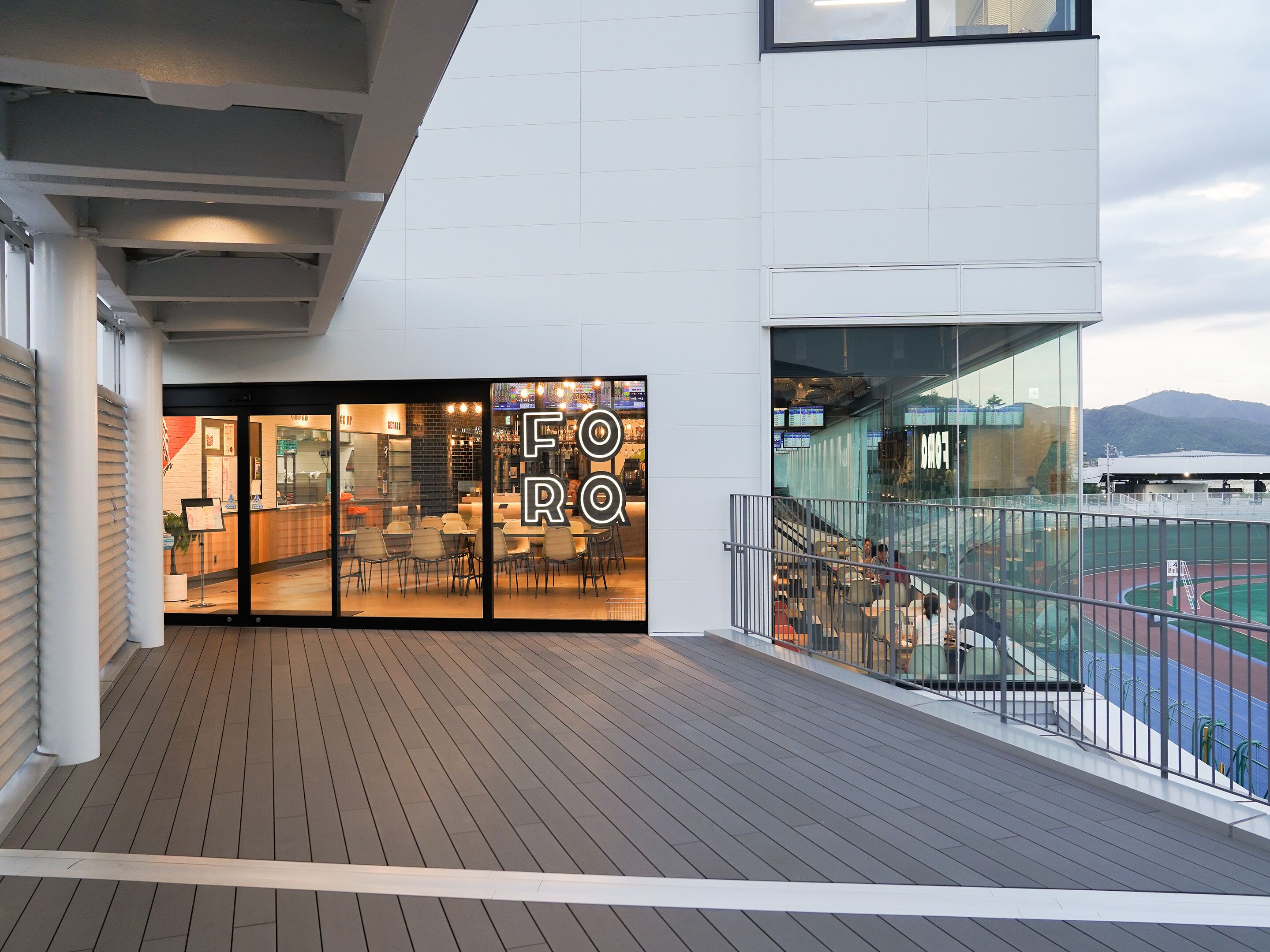 A restaurant with a modern design, featuring a wooden deck and a view of a sports field.