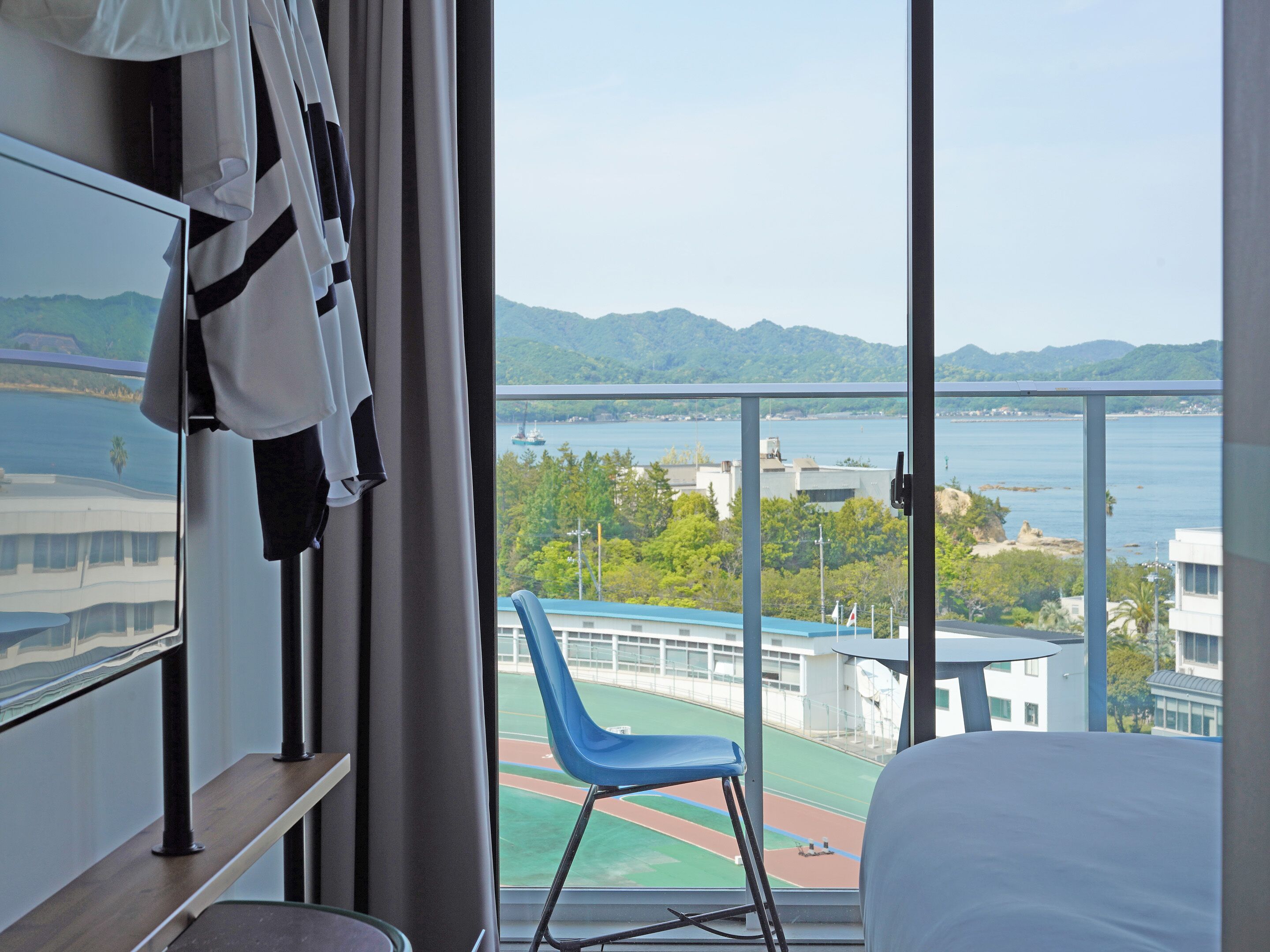 A hotel room with a large window offering a view of a sports field and a body of water.