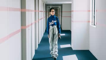 A person walking down a hallway with blue carpet and white walls, with a window on the right.