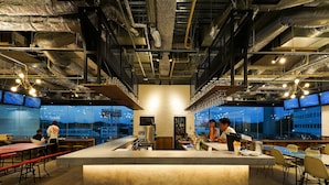 A modern bar area with a central counter, multiple seating options, and large windows offering a city view. - SETOUCHI KEIRIN HOTEL 10 by Onko Chishin (Tamano)