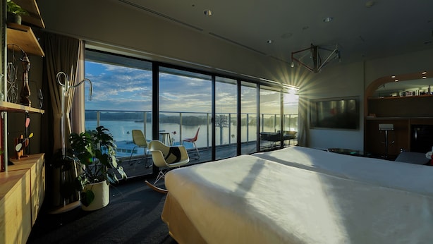 A modern hotel room with a large bed, a balcony with a view of the water, and a dining area with a table and chairs. - SETOUCHI KEIRIN HOTEL 10 by Onko Chishin (Tamano)