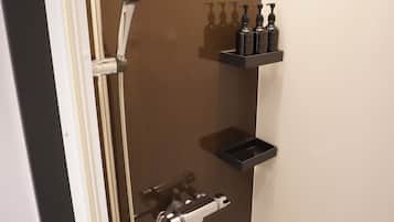 Ducha con cabezal de ducha de mano, grifo empotrado en la pared y un accesorio de ducha manual. Hay tres botellas negras sobre una estantería negra.