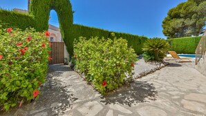 A stone pathway leading to a pool area with a wooden gate, surrounded by well-maintained hedges and flowering plants. - JUNAI, villa for 4 pax in Benissa with private swimming pool and free wifi (Benissa)