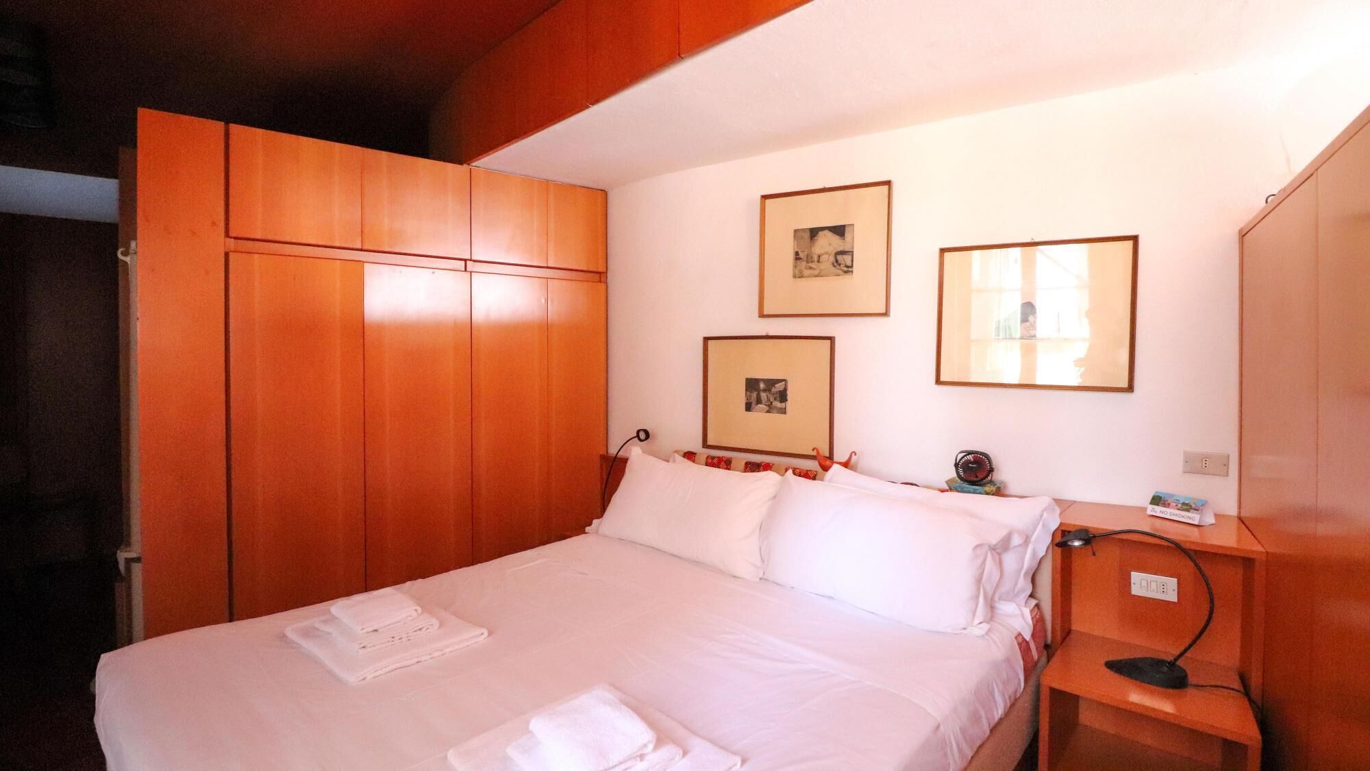 Une chambre d’hôtel avec un lit, une armoire en bois et deux tableaux encadrés accrochés au mur.