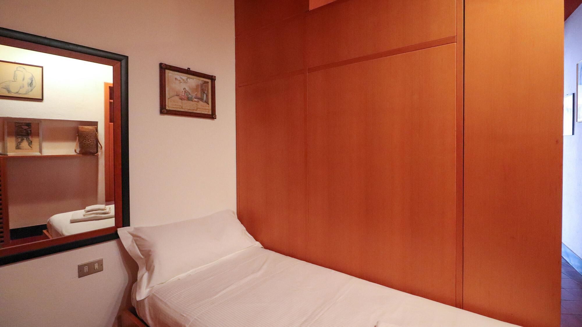 A single bed with a wooden headboard, a bedside table with a lamp, and a mirror on the wall.