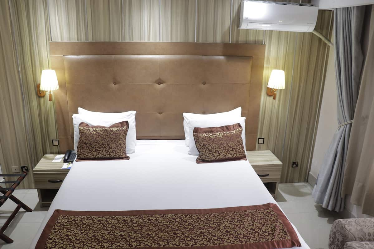 Quarto de hotel com uma cama grande, duas mesas de cabeceira, uma escrivaninha com cadeira e um ar condicionado.