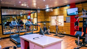 A gym with exercise equipment, a mirrored wall, and a television. - Golden Tulip Garden City Hotel - Rivotel (Port Harcourt)