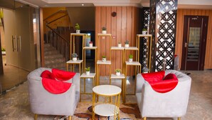 A modern lobby with a staircase, two grey armchairs with red throws, a central white round table, and a decorative wall with a geometric pattern. - Golden Tulip Garden City Hotel - Rivotel (Port Harcourt)