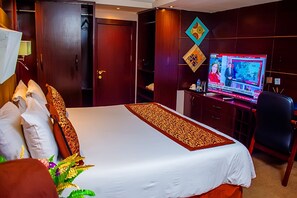 A hotel room with a large bed, a desk with a television, and a wardrobe. - Golden Tulip Garden City Hotel - Rivotel (Port Harcourt)