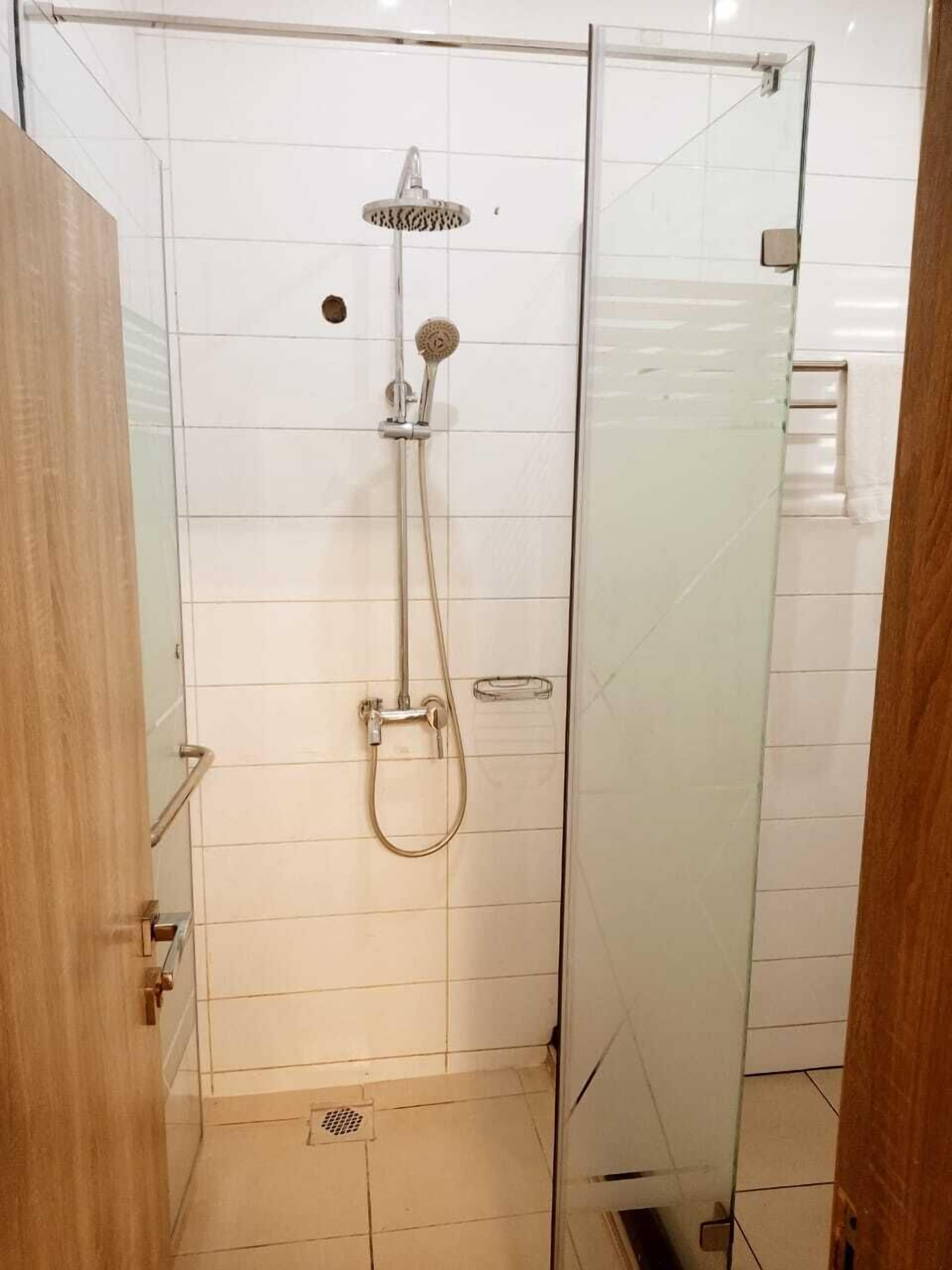 A glass-enclosed shower stall with a handheld showerhead and a wall-mounted showerhead.