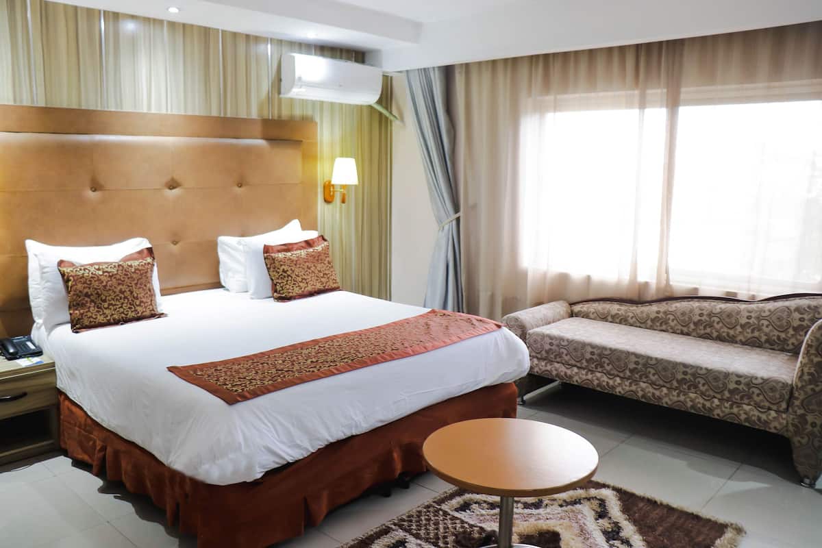 Quarto de hotel com uma cama grande, um sofá, uma mesinha e uma janela com cortinas.