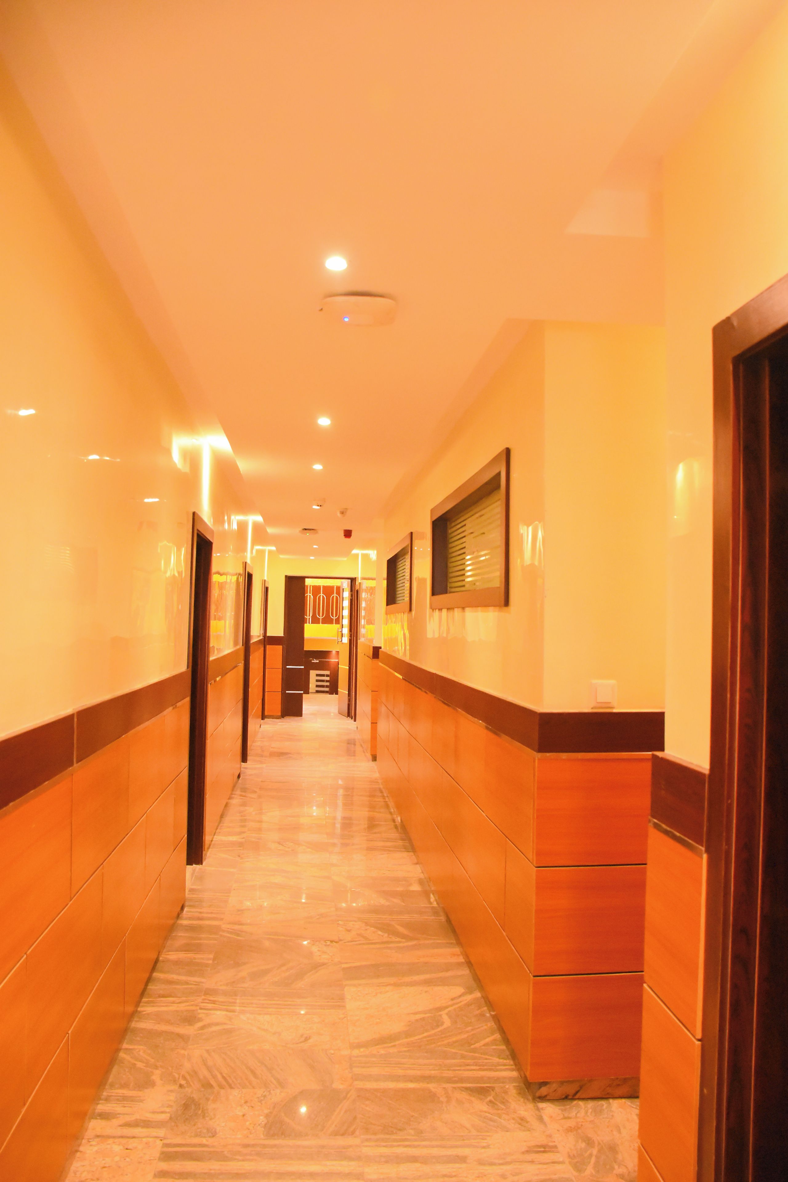 A corridor with a marble floor, recessed lighting, and a wooden door on the right.