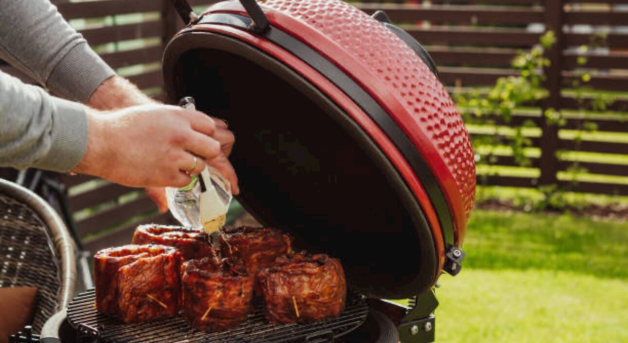 Una persona fent a la barbacoa carn en una barbacoa exterior amb un fumador vermell.