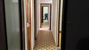 Un corridoio con pavimento a scacchi, porte in legno e una sedia in lontananza.
