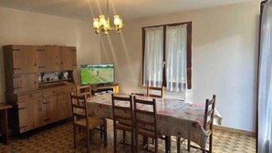 Zona pranzo con tavolo, sedie, televisore e pensili in legno.