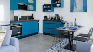 A modern kitchen with blue cabinets, a dining area with a table and chairs, and a painting of a whale on the wall. - Le Clos Moguer by Interhome (Quiberon)