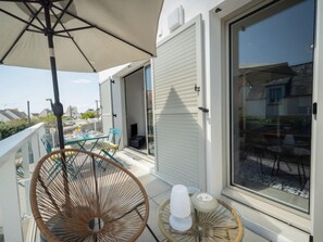 Ein Balkon mit Tisch und Stühlen, ein Korbstuhl, ein Tisch mit Kerze und ein großer Sonnenschirm.