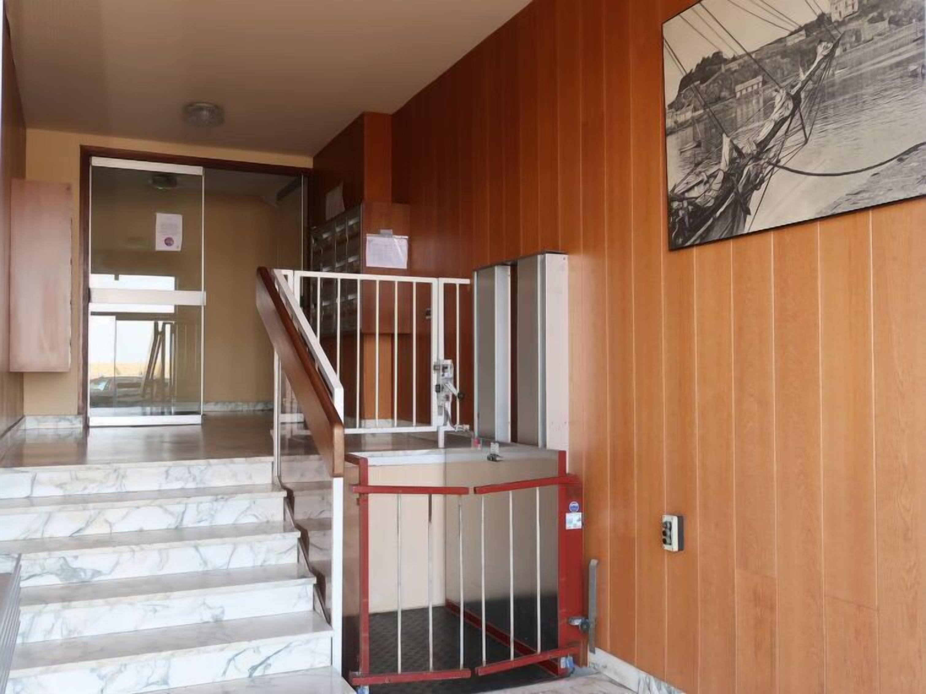 A staircase leading to a landing with a red gate, wooden paneling on the walls, and a painting above the gate.